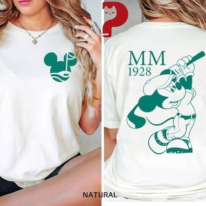 May include: Cream-colored t-shirt featuring a green Mickey Mouse golf design on the front and a baseball-themed Mickey Mouse graphic on the back. The back also displays "MM 1928" in green. The shirt is made of a soft, comfortable material.