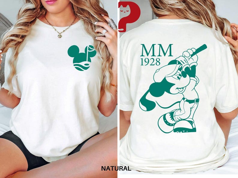 May include: Cream-colored t-shirt featuring a green Mickey Mouse golf design on the front and a baseball-themed Mickey Mouse graphic on the back. The back also displays "MM 1928" in green. The shirt is made of a soft, comfortable material.