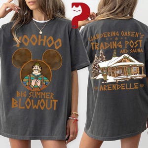 May include: Dark gray t-shirt with a front graphic featuring a cartoon character in a Mickey Mouse-shaped design, the text "Yoohoo Big Summer Blowout". The back of the shirt displays "Wandering Oaken's Trading Post and Sauna" with a cabin illustration.