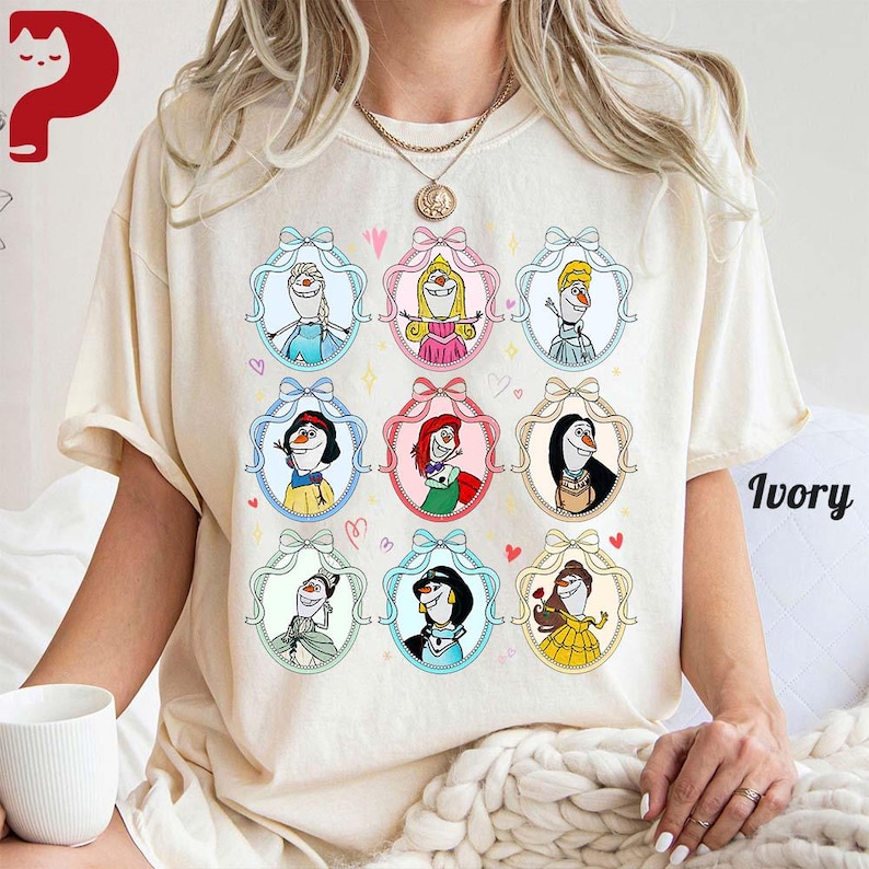 May include: Ivory-colored t-shirt featuring nine cartoon portraits of Disney characters in ornate frames. Each frame has a bow at the top and is surrounded by hearts. The word "Ivory" is printed in a script font on the lower right.