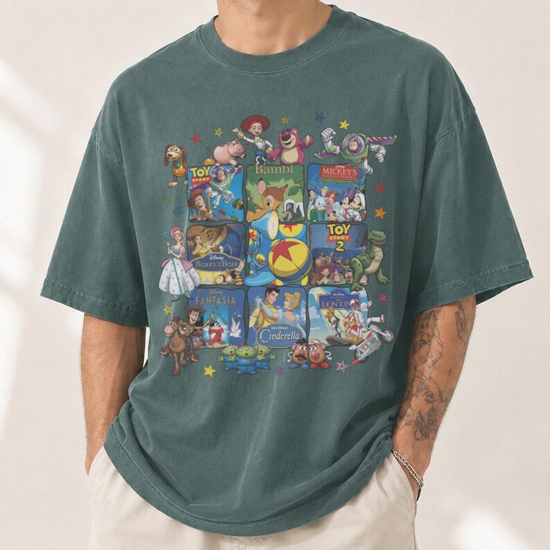 May include: Green t-shirt featuring a collage of classic Disney movie posters, including Toy Story, Bambi, and Cinderella. The design is surrounded by colorful stars. The shirt has short sleeves and a relaxed fit.