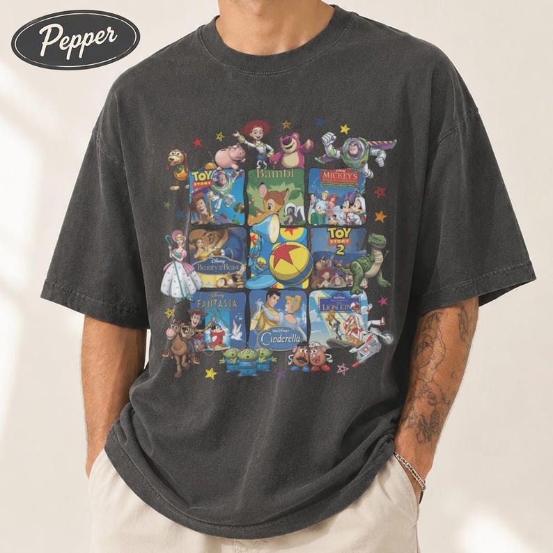 May include: Dark gray t-shirt featuring a collage of Disney movie posters, including Toy Story, Bambi, and Cinderella. The design is printed on a short-sleeved, crew neck shirt. The shirt has a vintage, faded look.
