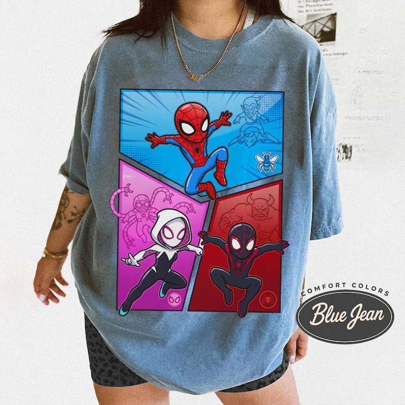 May include: Blue graphic t-shirt featuring a comic-style design with Spider-Man and other characters. The design is divided into four panels with a blue, red, and purple color scheme. The shirt has the text "Comfort Colors Blue Jean".