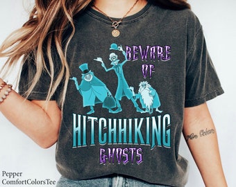 May include: A dark gray t-shirt with a graphic print of three ghosts. The text on the shirt reads "Beware of Hitchhiking Ghosts".
