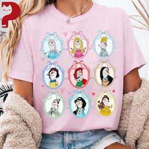 May include: Pink t-shirt featuring nine cartoon illustrations of characters in oval frames with bows. The characters include snowmen and princesses, each in a unique outfit. Hearts and stars are scattered around the frames.