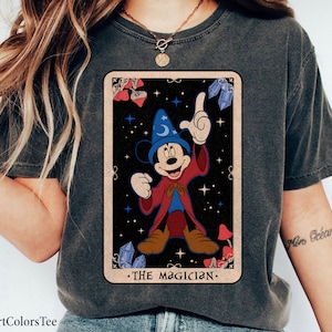 May include: A gray t-shirt with a vintage-style illustration of Mickey Mouse as a magician. The illustration is in a tarot card style with a black background and stars. The text "The Magician" is printed below the illustration.