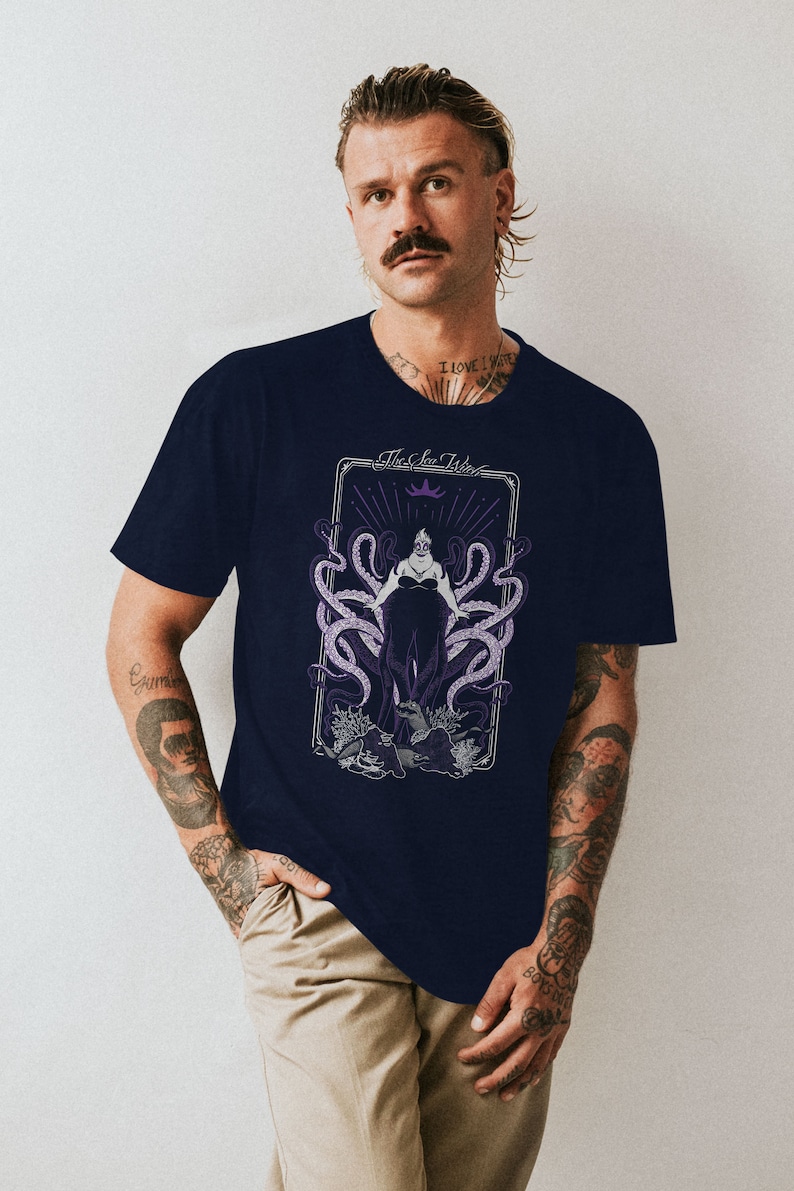 May include: A navy blue t-shirt with a graphic of Ursula, the sea witch from Disney's The Little Mermaid. The graphic is in a vintage tarot card style with the text "The Sea Witch".