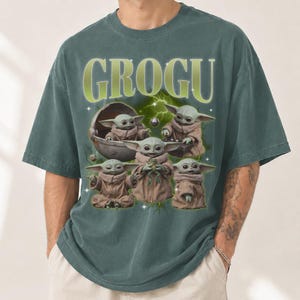 May include: Green t-shirt featuring the word "GROGU" in a light green font above a graphic of Grogu from The Mandalorian. The graphic shows Grogu in various poses, with a green and white background.
