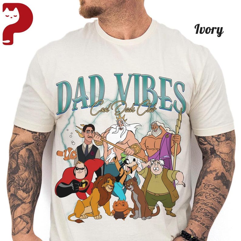 Peut inclure: T-shirt ivoire avec le texte "DAD VIBES Cool Dads Club" en bleu sarcelle et blanc. Le t-shirt pr&eacute;sente un graphisme de personnages de dessins anim&eacute;s. Le t-shirt est fait d'une mati&egrave;re douce.
