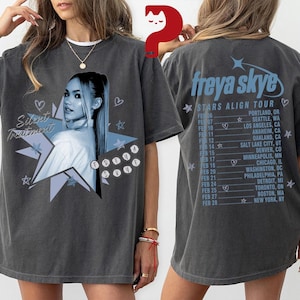 May include: Dark gray t-shirt featuring a portrait of Freya Skye in a blue and white graphic. The front of the shirt has the text "Silent Treatment". The back of the shirt lists tour dates and locations for the "Stars Align Tour".