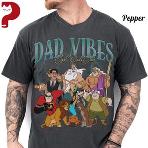 Peut inclure: T-shirt gris fonc&eacute; avec un col en V. Il pr&eacute;sente le texte "DAD VIBES Cool Dads Club" au-dessus d'un dessin anim&eacute; de divers personnages anim&eacute;s, dont Mr. Incredible et Simba.