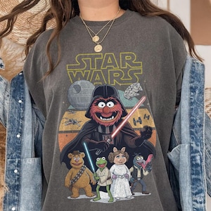 May include: Dark gray sweatshirt featuring a mashup of Star Wars and the Muppets. The design includes Darth Animal with a lightsaber, the Death Star, and other characters. The words "STAR WARS" are printed across the top.