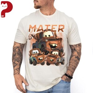 May include: Cream-colored t-shirt featuring a graphic of the character Mater from the movie Cars. The word "MATER" is printed above the image of the cartoon tow truck. The design includes three versions of Mater in different sizes.