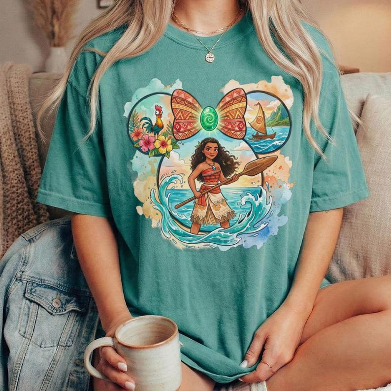 以下が含まれることがあります： ターコイズ色のTシャツ。カラフルなグラフィックは、パドルを持つキャラクターが特徴で、雄鶏、花、帆船の付いたリボン型のデザインに囲まれています。キャラクターは青と白の波の中に立っています。
