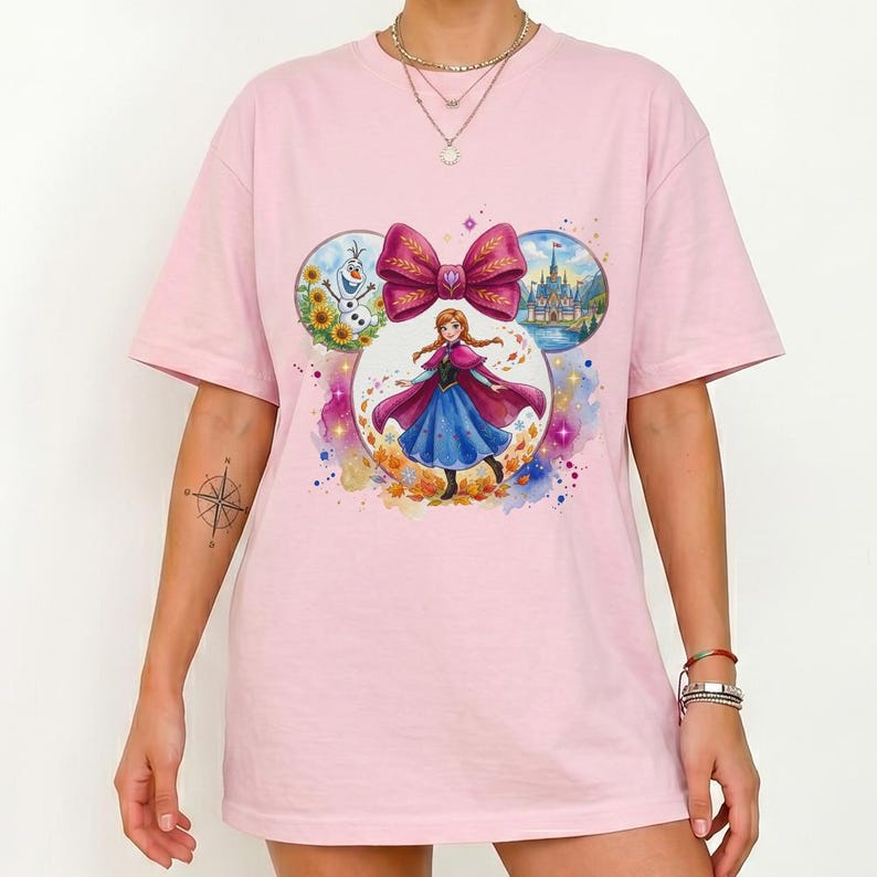 Puede incluir: Camiseta rosa claro con un gr&aacute;fico colorido de un personaje de una popular pel&iacute;cula animada. El gr&aacute;fico incluye un gran lazo, un personaje con un vestido azul y una capa roja, y otros elementos animados.
