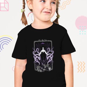 May include: A black t-shirt with a graphic of Ursula, the Sea Witch, from Disney's The Little Mermaid. The graphic is in a vintage style with a purple and white color scheme. The text "The Sea Witch" is above the graphic.
