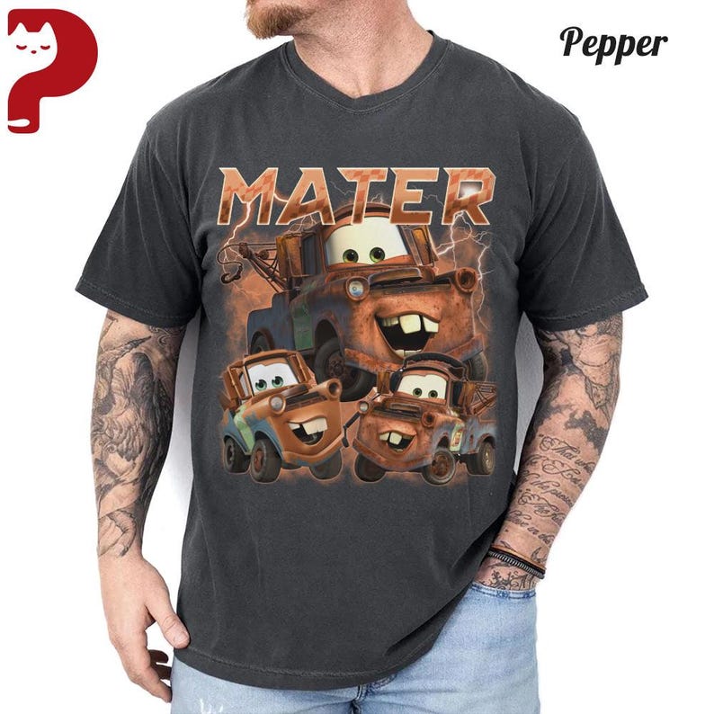May include: Dark gray t-shirt featuring a graphic of the character Mater from the movie Cars. The design includes the word "MATER" in orange lettering above the character's image. The shirt has a V-neck.