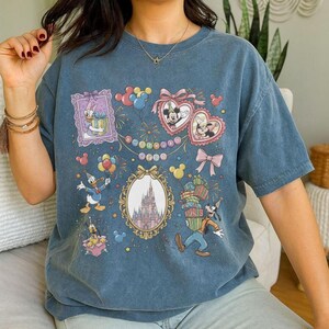 May include: Blue t-shirt featuring Disney characters like Mickey and Minnie Mouse, Donald Duck, and Goofy. The shirt has a birthday theme with balloons, gifts, and a castle illustration. The word "Birthday" is also visible.