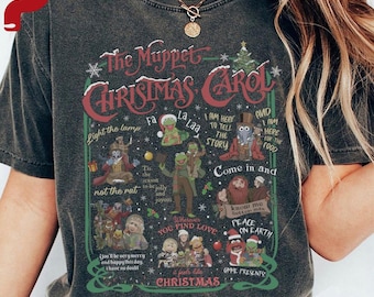 Op de afbeelding: Donkergrijs T-shirt met een afbeelding van "The Muppet Christmas Carol". Het ontwerp bevat verschillende Muppet-personages en zinnen als "Peace on Earth" en "Christmas". Het shirt heeft een vintage, versleten uitstraling.