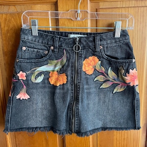 May include: Black denim mini skirt with a floral print and a zip closure. The skirt has a frayed hem.
