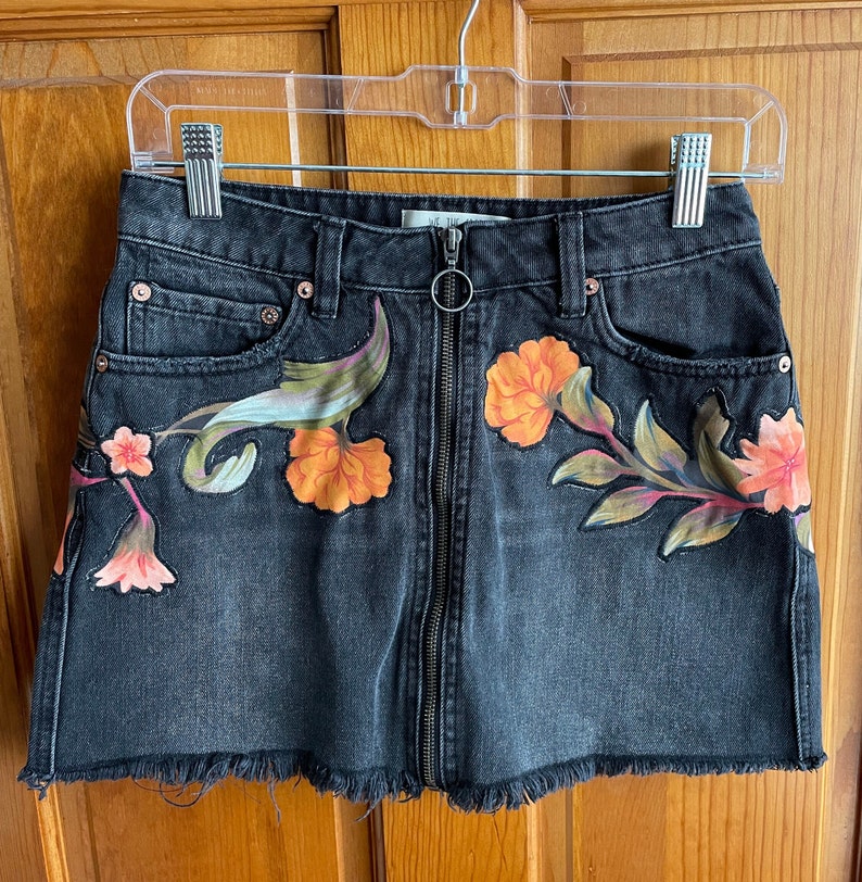 May include: Black denim mini skirt with a floral print and a zip closure. The skirt has a frayed hem.
