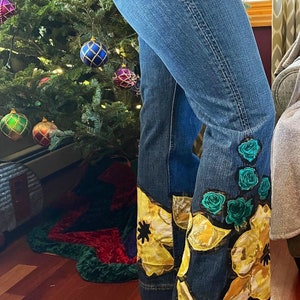 May include: Blue denim jeans with yellow and green floral embroidery on the bottom of the legs.