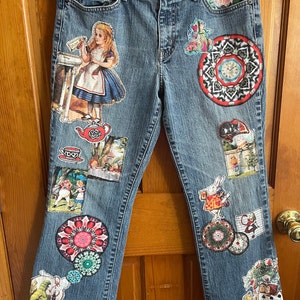May include: Blue denim jeans with various Alice in Wonderland themed patches, including Alice holding a teacup, the Mad Hatter, the Queen of Hearts, and a teapot.
