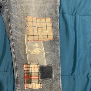 May include: Blue denim jeans with multiple patches sewn on. The patches are made of different plaid fabrics in red, white, and blue.