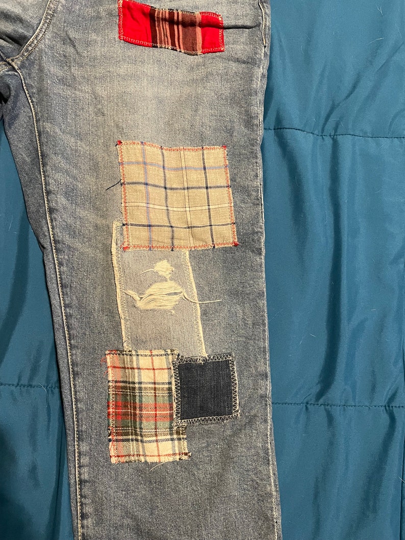 May include: Blue denim jeans with multiple patches sewn on. The patches are made of different plaid fabrics in red, white, and blue.