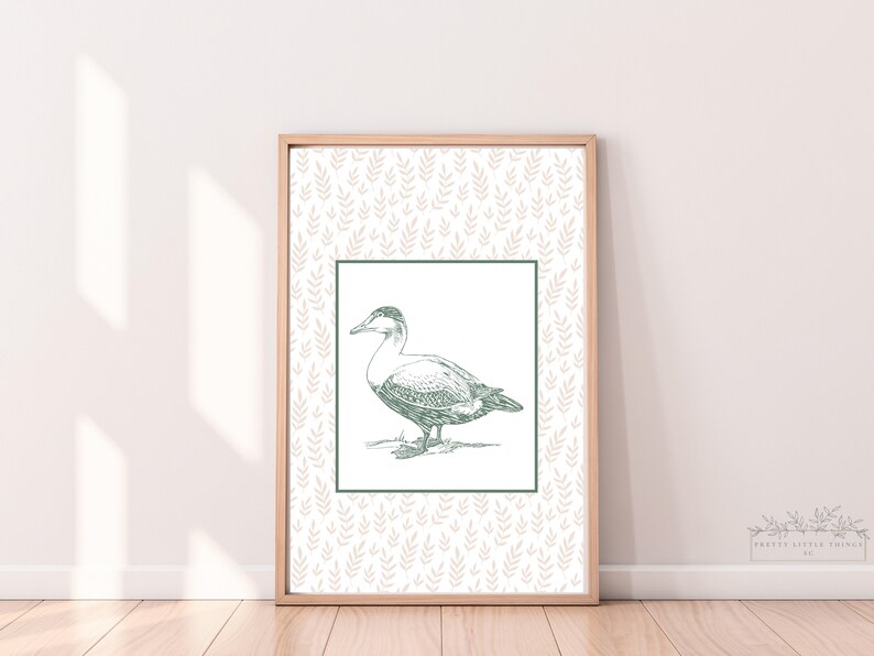 May include: A framed print with a green line drawing of a duck on a white background. The background of the print is a light pink pattern of leaves.