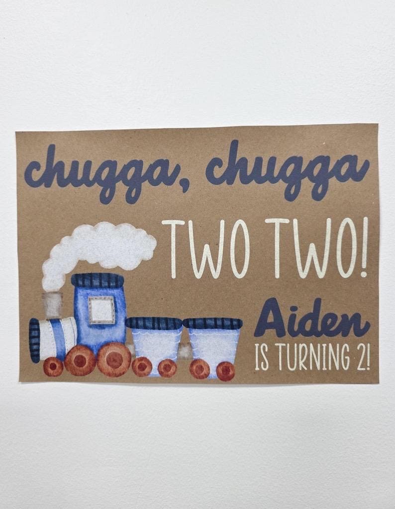 May include: A brown card with a watercolor illustration of a blue train with white smoke. The text "chugga, chugga TWO TWO! Aiden IS TURNING 2!" is written in blue and white.