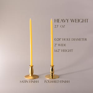 May include: Two gold metal candle holders with yellow taper candles. One has a satin finish and the other a polished finish. Text reads: HEAVY WEIGHT, 2.7 OZ, 0.28" HOLE DIAMETER, 2" WIDE, 1.62" HEIGHT, SATIN FINISH, POLISHED FINISH.