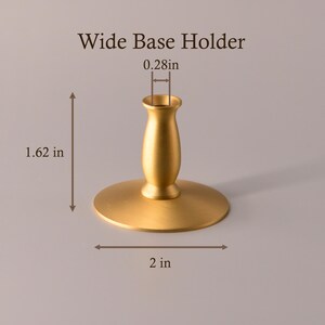 May include: A gold-colored metal candle holder labeled Wide Base Holder. The object features a wide circular base and a central stem. Dimensions shown are 1.62 inches in height, a 2-inch base diameter, and a 0.28-inch opening for a candle.