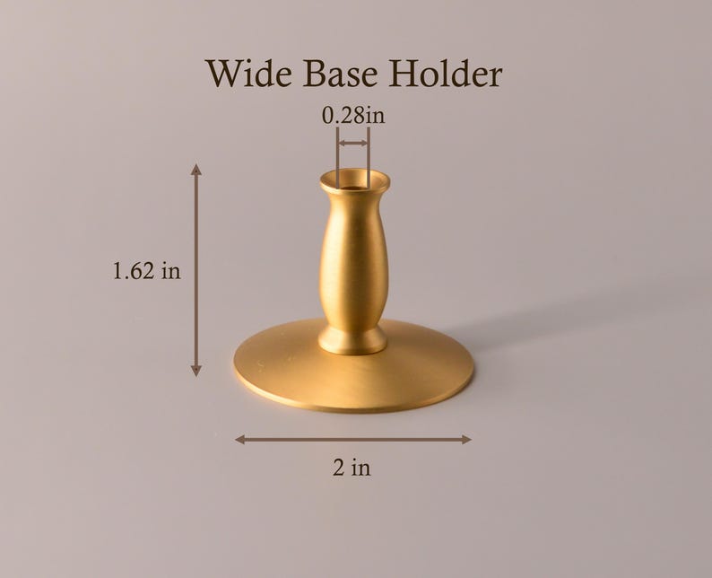 May include: A gold-colored metal candle holder labeled Wide Base Holder. The object features a wide circular base and a central stem. Dimensions shown are 1.62 inches in height, a 2-inch base diameter, and a 0.28-inch opening for a candle.