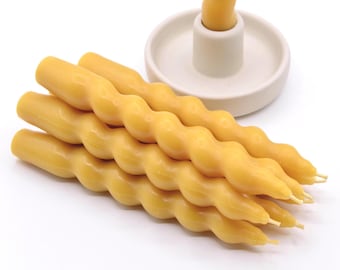 May include: A set of five yellow beeswax candles with a twisted, wavy design. The candles are arranged in a stack, with the tips of the candles pointing to the right.