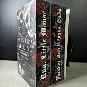 May include: Two books titled Haunting Adeline by H.D. Carlton with black covers featuring a skull, red roses, and white butterflies. The page edges are printed with a spiderweb pattern, red roses, and the text Run, Little Mouse and Forever And Always, Baby.
