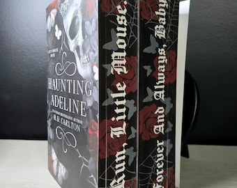 May include: Two books with black covers featuring a skull, red roses, and white butterflies. The first book is titled Haunting Adeline by H.D. Carlton. The page edges are printed with the text Run, Little Mouse and Forever And Always, Baby.