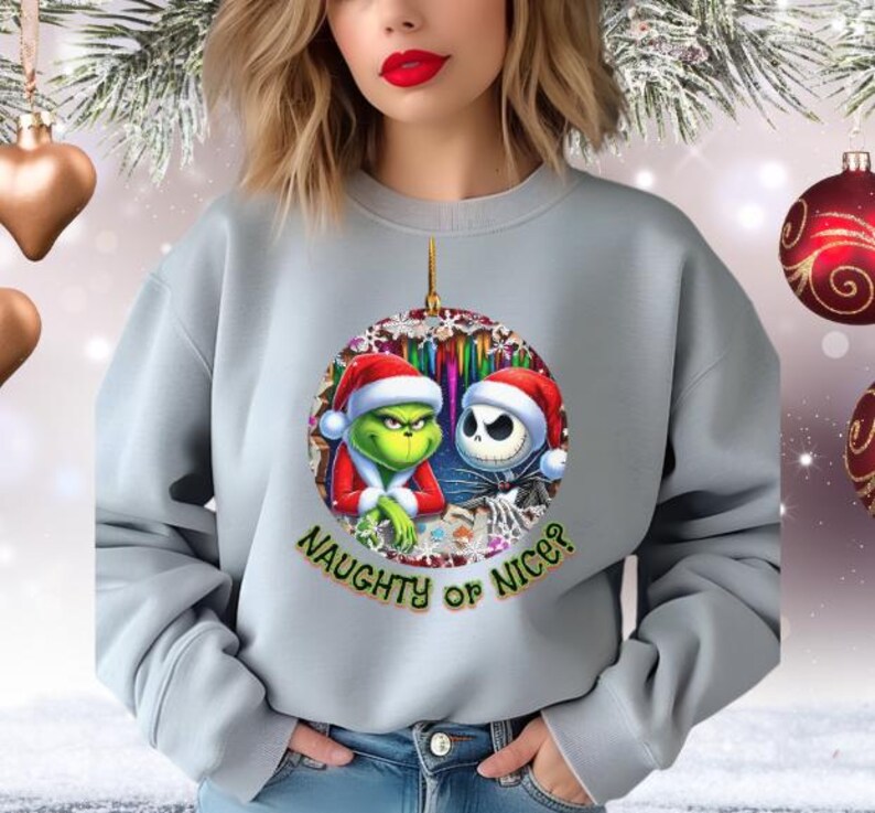 Puede incluir: Una sudadera gris claro con un dise&ntilde;o de adorno navide&ntilde;o con el Grinch y Jack Skellington con gorros de Pap&aacute; Noel. El adorno tiene el texto "NAUGHTY OR NICE?" en verde. La sudadera la lleva una persona.