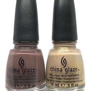 May include: Two bottles of China Glaze nail polish. One is a muted mauve color, the other is a shimmering gold. Both have black caps and labels with the brand name and product information. Each bottle contains 14 mL or .5 fl oz of polish.