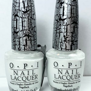 May include: Two O.P.I Nail Lacquer bottles with white polish. The bottles have silver and black textured caps. Each bottle has the text "O.P.I NAIL LACQUER" printed on the front. The bottles contain 15 mL or 0.5 fl oz of nail polish.