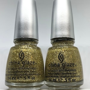 May include: Two bottles of China Glaze nail lacquer with a gold glitter finish. Each bottle has a silver cap and contains 14 ml or .5 fl oz of product. The bottles are labeled with the brand name and product details.