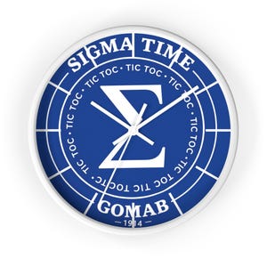 May include: White wall clock with a blue face featuring the text "SIGMA TIME" and "TIC TOC" around the edge. The clock face has a white Greek letter symbol and the text "GOMAB - 1914".