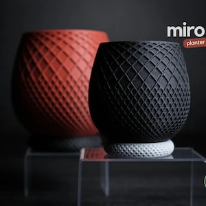May include: Two decorative planters, one red and one black, with a geometric lattice design. The planters are on clear stands. The word "miro" and the word "planter" are in the image.