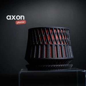 May include: Black planter with a geometric design and a red interior. The planter has a unique shape and sits on a matching saucer. The word "axon" and "planter" are displayed in the upper left corner.