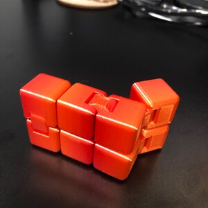 Op de afbeelding: Een feloranje 3D-geprint puzzelspeelgoed met een uniek ontwerp. De puzzel bestaat uit meerdere verbonden kubussen die kunnen worden gedraaid en gemanipuleerd.