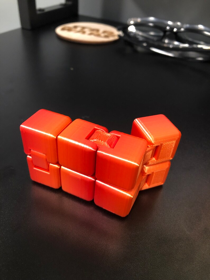 Op de afbeelding: Een feloranje 3D-geprint puzzelspeelgoed met een uniek ontwerp. De puzzel bestaat uit meerdere verbonden kubussen die kunnen worden gedraaid en gemanipuleerd.