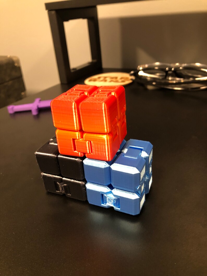 Op de afbeelding: Een stapel van drie fidget cubes in rood, zwart en blauw. De kubussen zijn gemaakt van plastic en hebben een getextureerd oppervlak.
