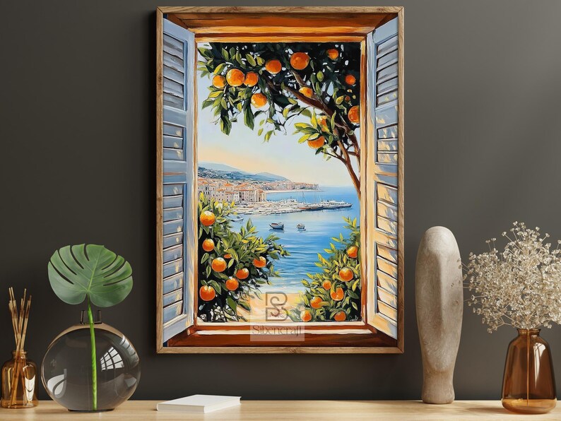 Op de afbeelding: Een ingelijst schilderij toont een kustlandschap door een raam met blauwe luiken. Sinaasappelbomen omlijsten het uitzicht op een blauwe zee, boten en een verre stad. Het kunstwerk heeft een warm, uitnodigend kleurenpalet.