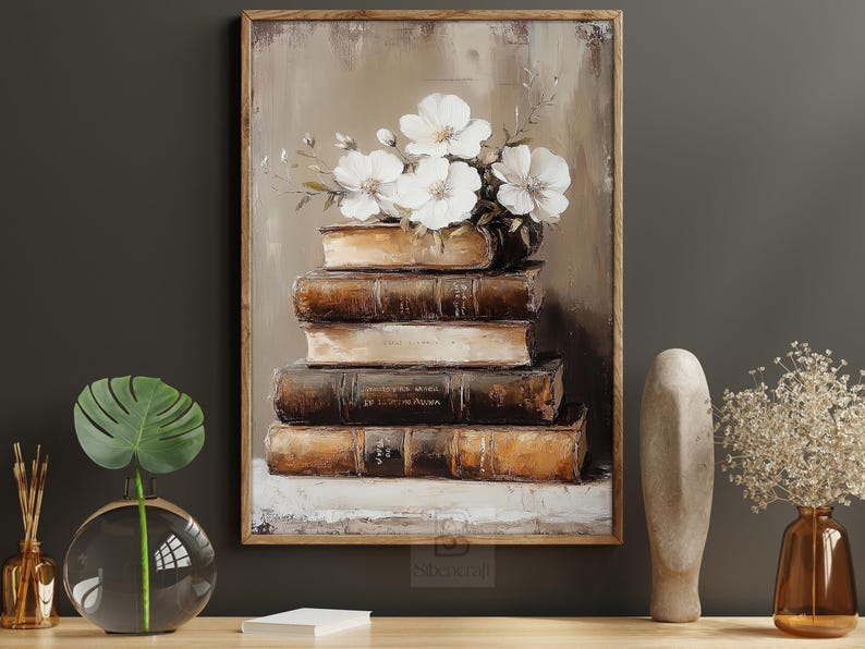 May include: An oil painting depicts a stack of antique books topped with white flowers. The books are brown and beige, with visible text on the spines. The artwork is framed in a wooden frame and has a neutral color palette.