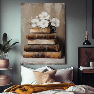 May include: An oil painting depicts a stack of aged books topped with a vase of white flowers. The books are brown and beige, with visible wear and tear. The artwork hangs above a bed with white pillows and a mustard-colored blanket. A potted plant sits on a side table.